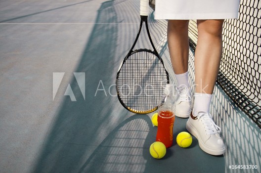 Picture of Tennis concept woman legs next to tennis balls and refreshing drink next to net copy space outdoors 